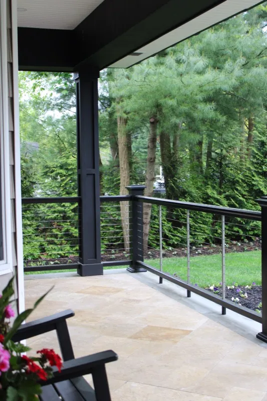 Covered porch with cable railing and stone flooring by Alec's Construction