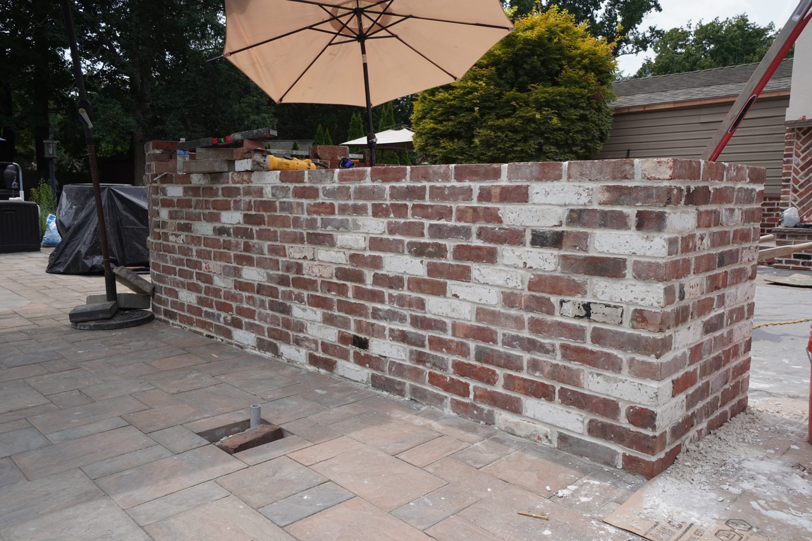 Curved reclaimed-brick outdoor kitchen wall beside paver patio and pool